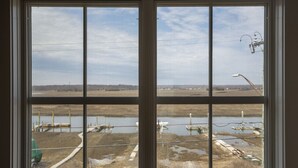 Blick durch ein Fenster auf einen klaren Himmel, ein Gewässer und einige Industriegebäude.