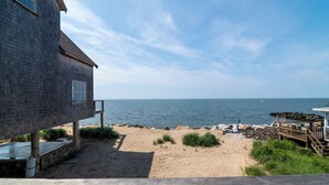 Ein Strandhaus mit Meerblick, einem Sandstrand und einer Holzterrasse.
