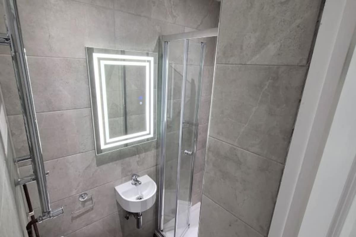 A modern bathroom with a glass shower enclosure, a pedestal sink, and a wall-mounted mirror with a light.