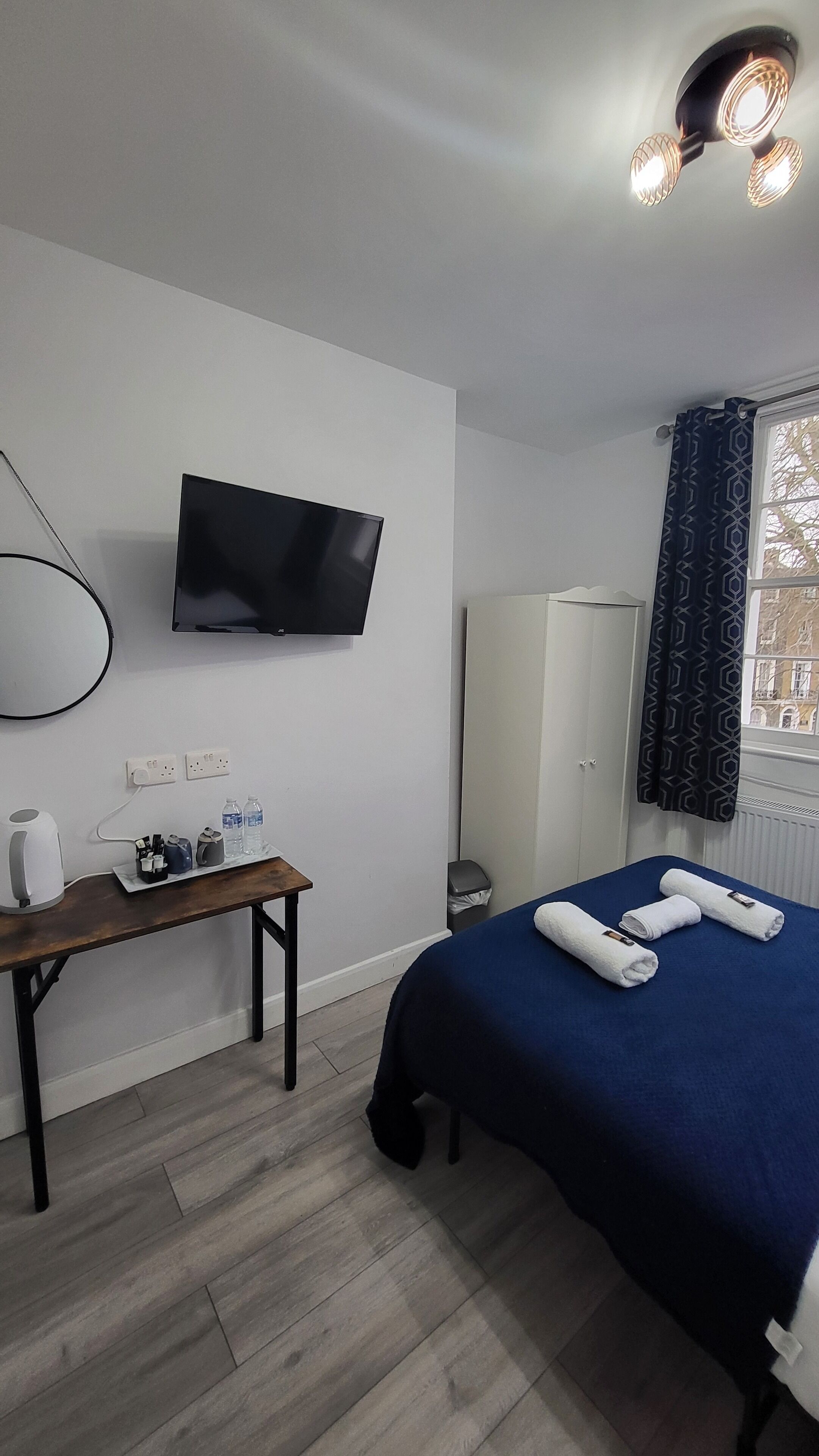 A hotel room with a bed, a desk with a kettle, a TV, and a wardrobe.