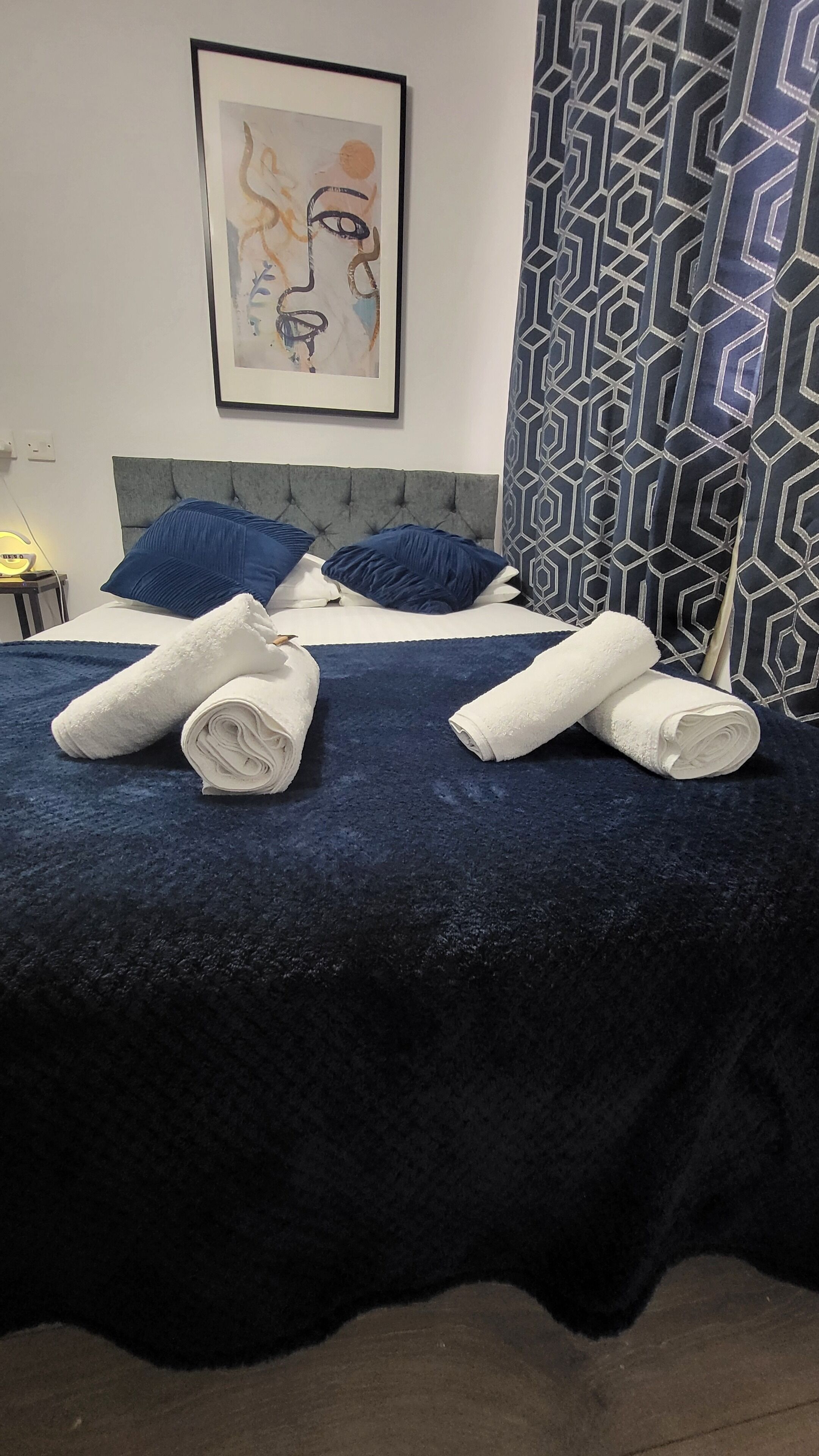 A neatly made bed with a blue bedspread and two rolled white towels.