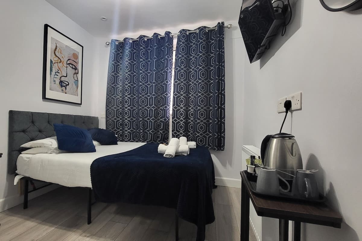 Habitación de hotel moderna con una cama bien hecha, una mesita de noche con lámpara, un hervidor y una pequeña mesa con artículos de aseo.