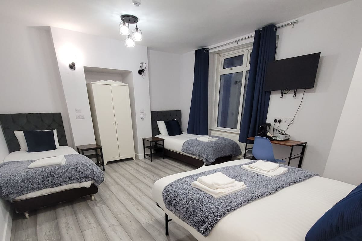 Habitación de hotel con dos camas, un armario, un escritorio con silla, un televisor y una ventana con cortinas.