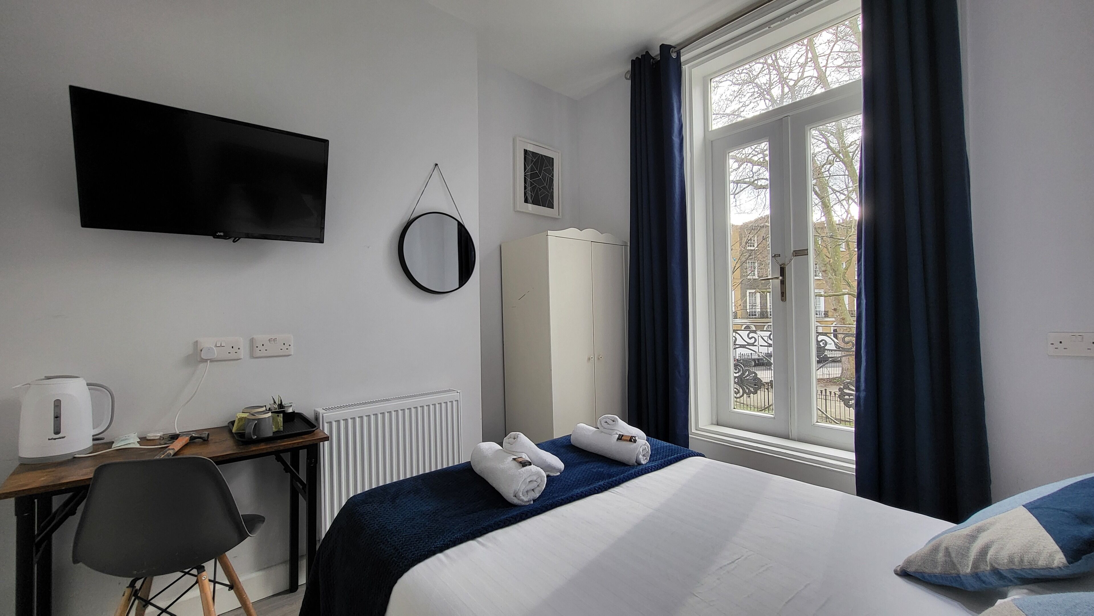 Een hotelkamer met een bed, een bureau met waterkoker, een televisie en een kledingkast.