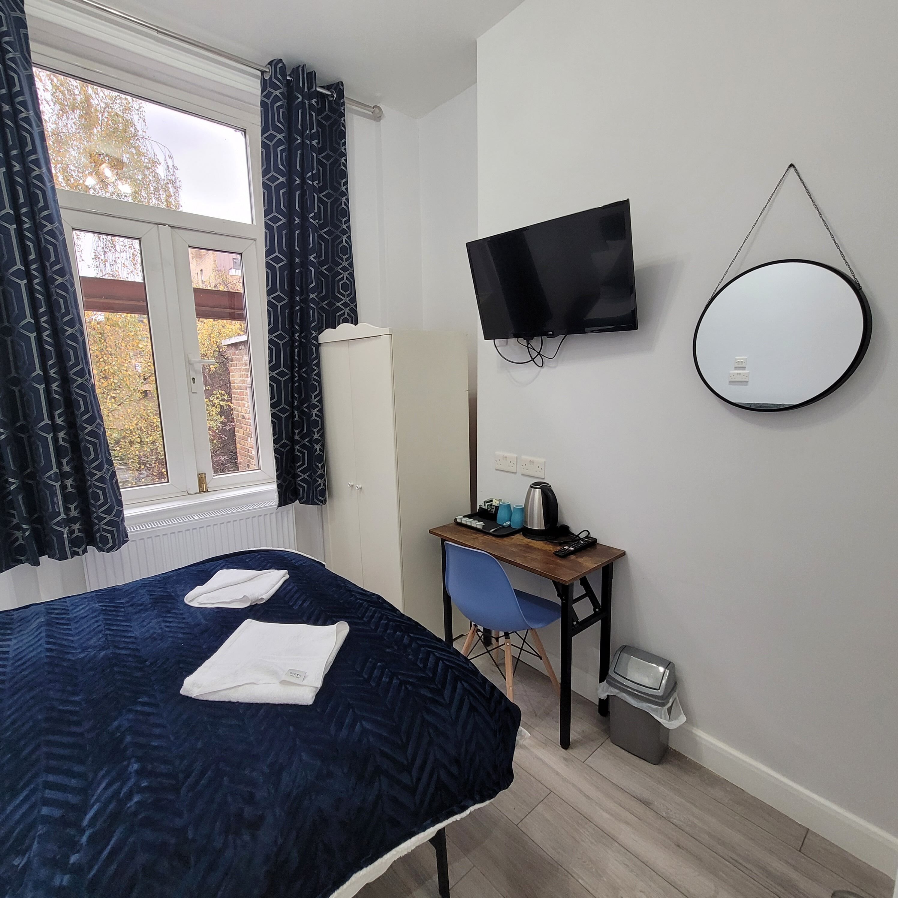 A bedroom with a bed, a desk, a chair, a TV, and a mirror.