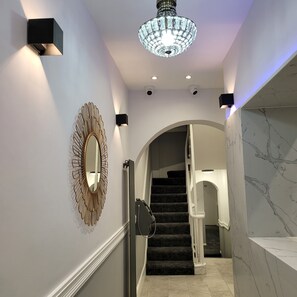 A modern interior with a marble staircase, a chandelier, and wall-mounted sconces. - Argyle Square Hotel (London)