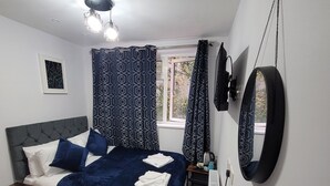 Un dormitorio con una cama, una mesita de noche, un espejo y una ventana con cortinas.