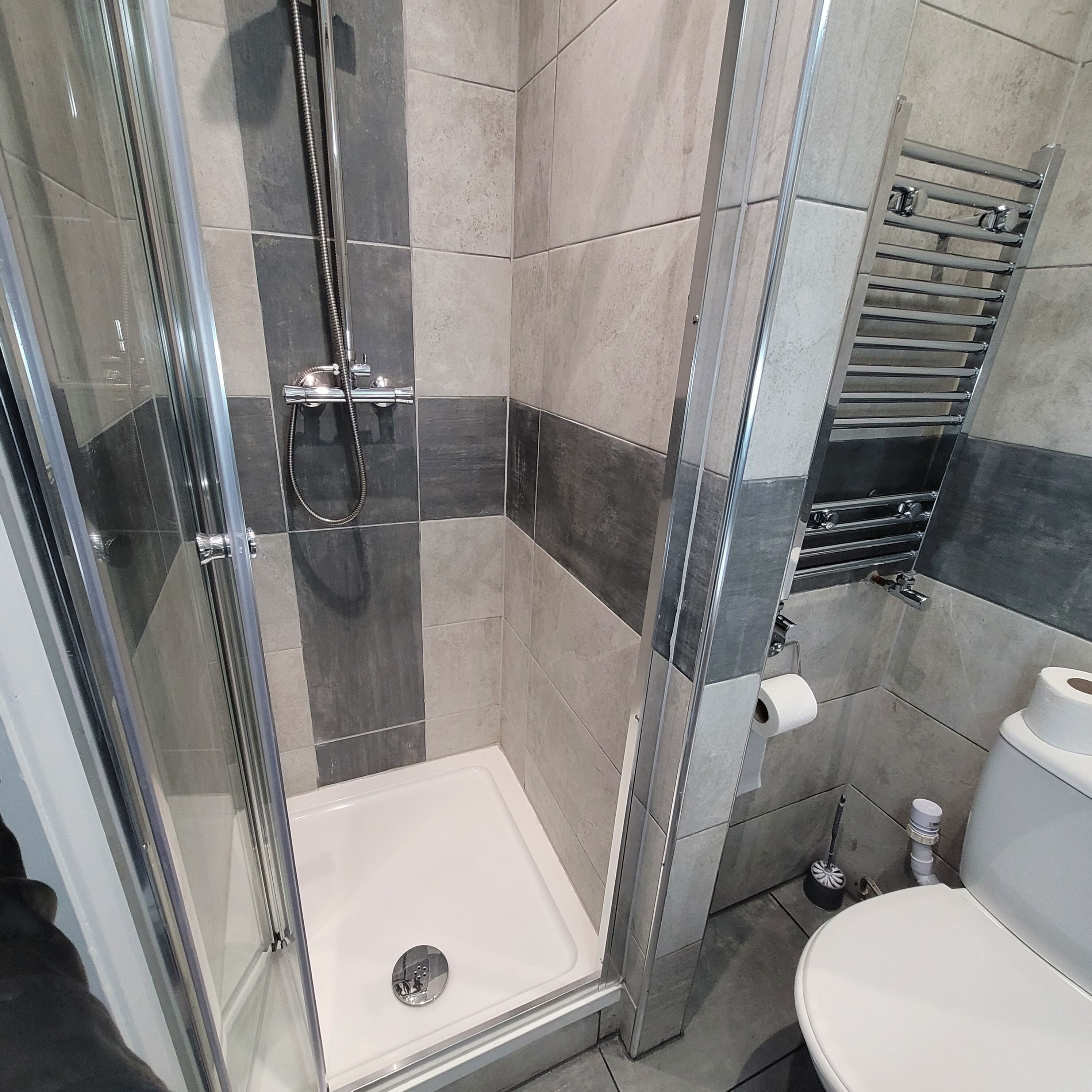 Een moderne badkamer met een douchecabine van glas, een wit toilet en een handdoekrek.