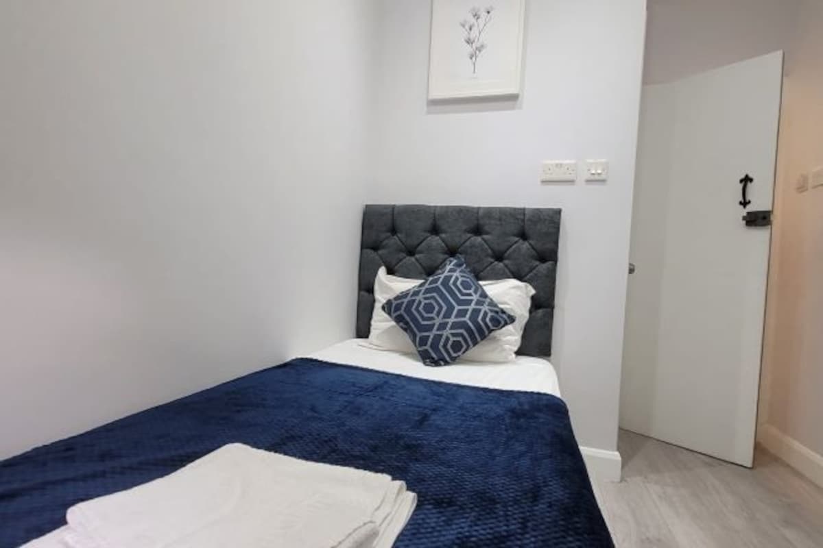 A bedroom with a tufted headboard, a blue and white bedspread, and a white blanket on the bed.