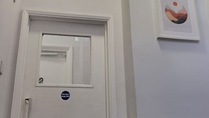 Una puerta blanca con un cartel que indica 'mantenga la puerta cortafuegos cerrada', una ventana con diseño de cuadrícula y un cuadro en la pared.
