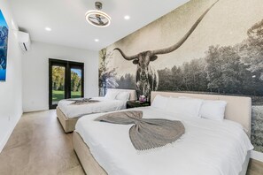 Quarto moderno com duas camas, um grande mural de um touro e vista para uma paisagem verde através de uma porta deslizante.