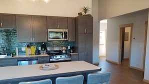 A modern kitchen with dark cabinets, stainless steel appliances, and a central island with bar stools. - Alderwood Cabin - Homer Seaplane Base (Homer)