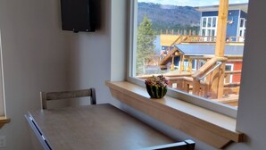 A dining area with a table and chairs, a window with a view of buildings and a wooden structure, and a mounted television. - Dockside Cabin - Homer Seaplane Base (Homer)