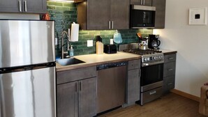 A modern kitchen with stainless steel appliances, dark wooden cabinets, and a green tiled backsplash. - Dockside Cabin - Homer Seaplane Base (Homer)