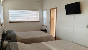 Quarto com duas camas, televisão na parede e janela com persianas.