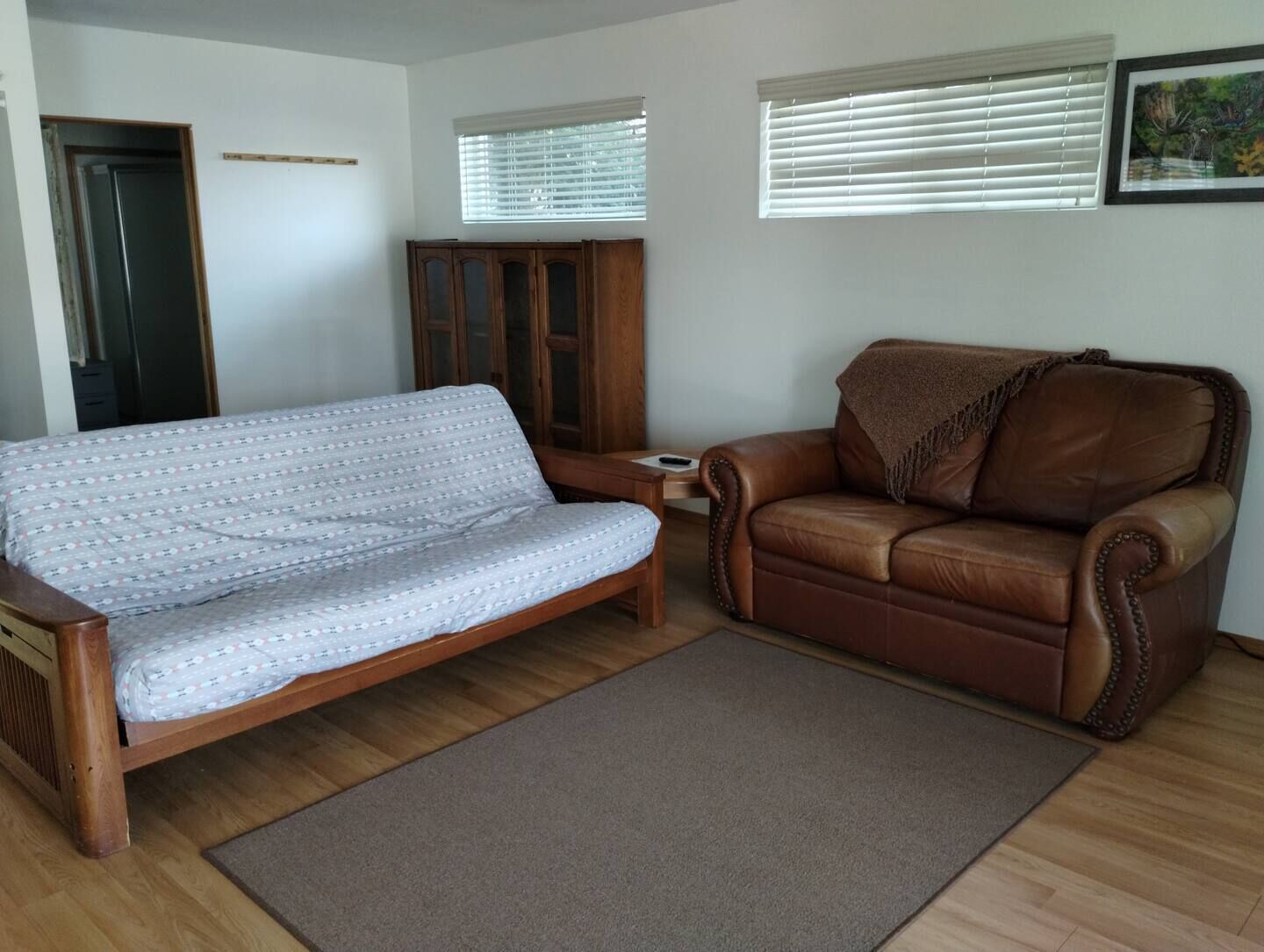 Una sala de estar con un sofá, un sillón de cuero, un aparador de madera y una puerta.
