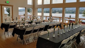 Une salle de conférence dotée de plusieurs tables et chaises, de grandes fenêtres offrant une vue sur un lac et des montagnes, et d’un panneau indiquant la sortie sur le mur.