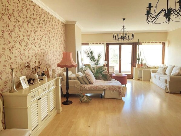 A spacious living room with a sofa set, a coffee table, a floor lamp, and a large window with curtains.