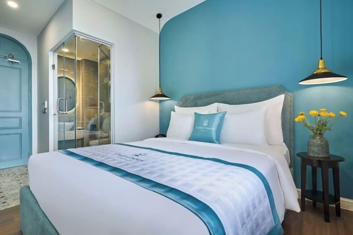 A bedroom with a large bed, a glass shower enclosure, and a blue accent wall.
