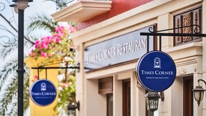 A Times Corner Restaurant sign with a blue circular logo and a decorative lamp post. - Times Corner Sorrento Boutique Hotel (Phu Quoc)