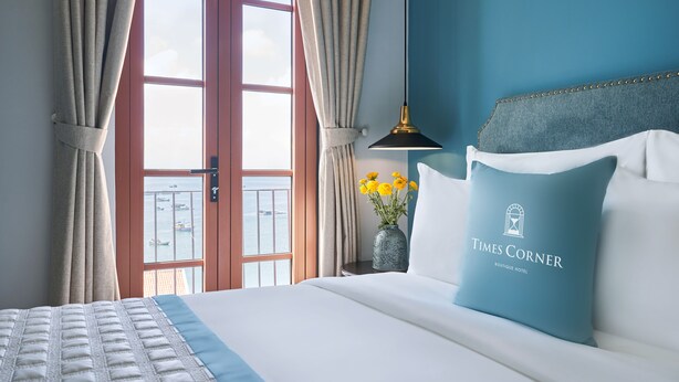A hotel room with a bed, a vase with flowers, and a view of the sea. - Times Corner Sorrento Boutique Hotel (Phu Quoc)