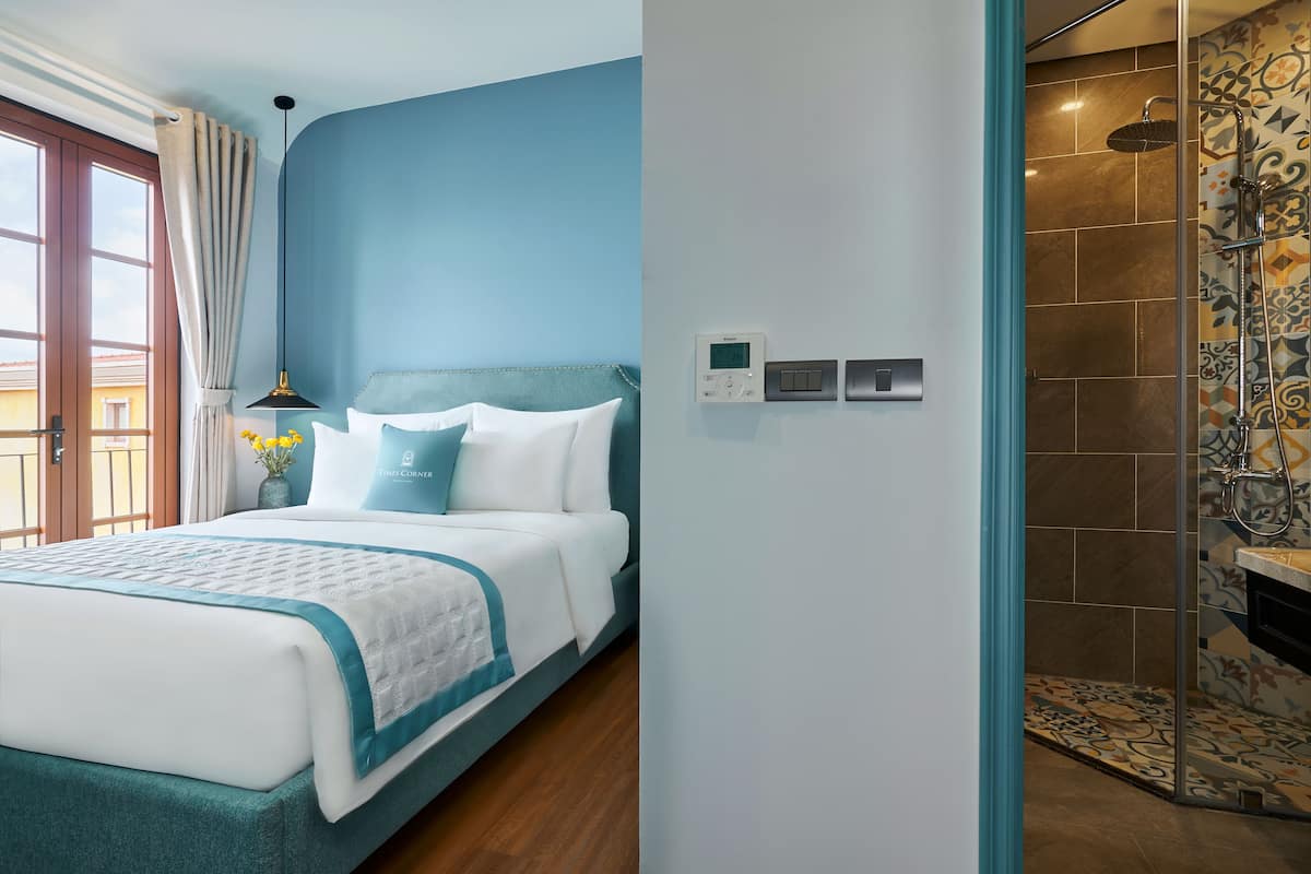 A bedroom with a bed, a bedside table with a lamp, a wall-mounted thermostat, and a shower area with a tiled wall.