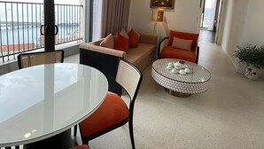 A modern living room with a glass dining table, orange chairs, a sofa with red cushions, a patterned coffee table, and a painting on the wall. - Times Corner Sorrento Boutique Hotel (Phu Quoc)