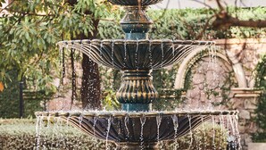 A multi-tiered fountain with water cascading down, surrounded by greenery and a stone wall. - Times Corner Sorrento Boutique Hotel (Phu Quoc)
