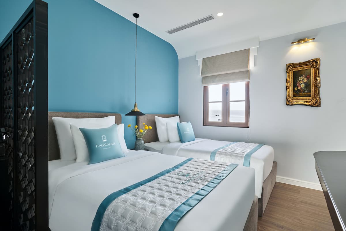 A hotel room with two beds, a large window, a painting, and a desk.