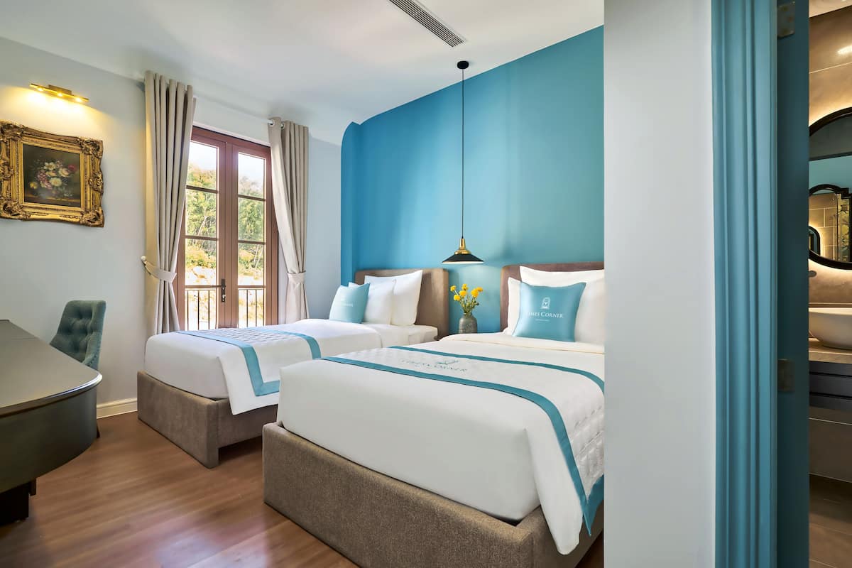 A hotel room with two beds, a desk, and a window with curtains.