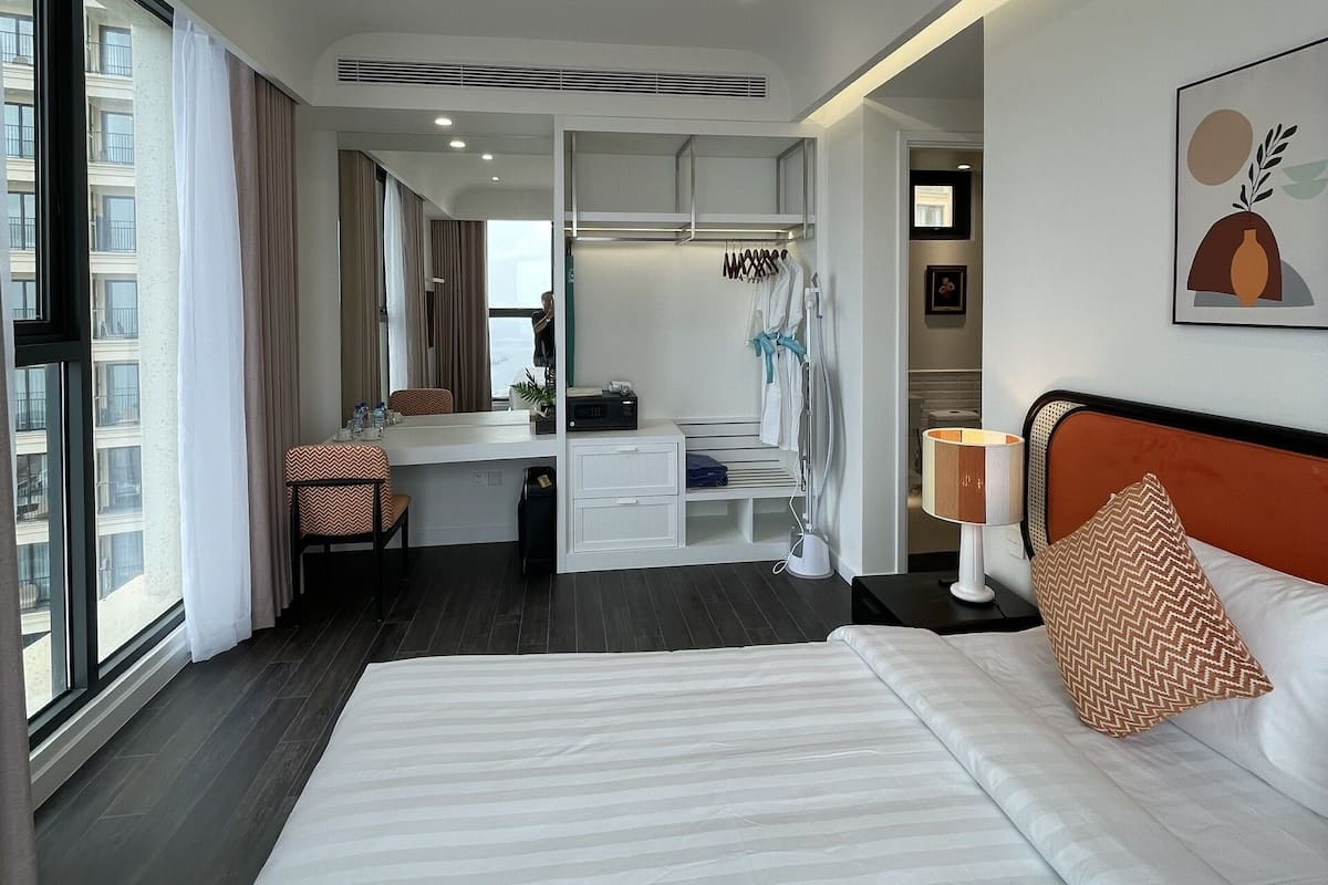 A modern hotel room with a large bed, a desk, and a walk-in closet.