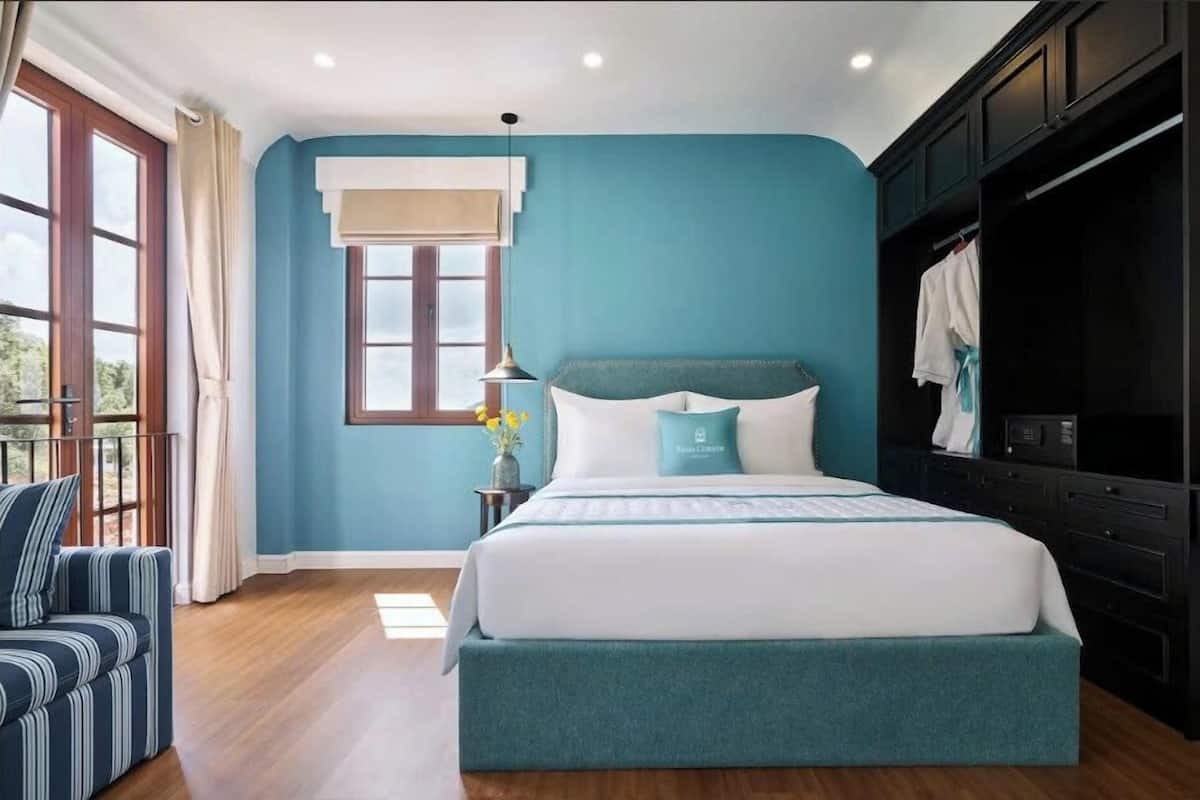 A bedroom with a large bed, a nightstand, a window with curtains, a sofa, and a wardrobe.