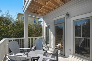 A covered outdoor deck with Adirondack chairs and a table, large windows, and a view of neighboring buildings. - 30A Retreat-Beach Access Nearby-Comm Pools-4 Bikes (Santa Rosa Beach)