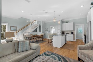 A spacious living area with a sofa, a dining table, and a kitchen with white cabinets and a central island. - 30A Retreat-Beach Access Nearby-Comm Pools-4 Bikes (Santa Rosa Beach)