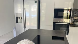 A modern kitchen with stainless steel appliances, a central island with a vase of white flowers, and a built-in oven. - Beautiful contemporary apartment in the heart of Rodney Bay! (Rodney Bay)