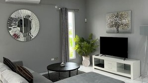 A modern living room with a grey sofa, a round mirror, a flat-screen TV, and a potted plant. - Beautiful contemporary apartment in the heart of Rodney Bay! (Rodney Bay)
