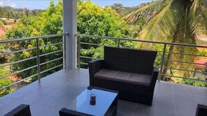 A balcony with a sofa and a small table, surrounded by metal railings and lush greenery. - Beautiful contemporary apartment in the heart of Rodney Bay! (Rodney Bay)