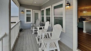A covered porch with white Adirondack chairs, a wooden deck, and a view of the ocean. - Sassy Seahorse by Silver Sands Vacation Rentals (Port Aransas)