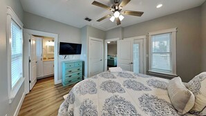 A bedroom with a bed, a ceiling fan, a TV, and a bathroom visible through an open door. - Sassy Seahorse by Silver Sands Vacation Rentals (Port Aransas)