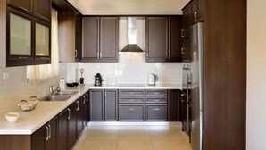A modern kitchen with dark wooden cabinets, a stainless steel refrigerator, and a central island with a sink and kettle. - ELIA KOUNOUPIDIANA (Chania)