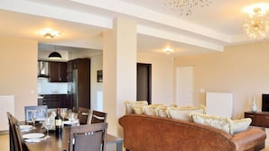 A modern living room with a brown sofa, dining table with chairs, and a kitchen in the background. - ELIA KOUNOUPIDIANA (Chania)