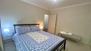A bedroom with a bed, bedside table, lamp, and a bench with towels.