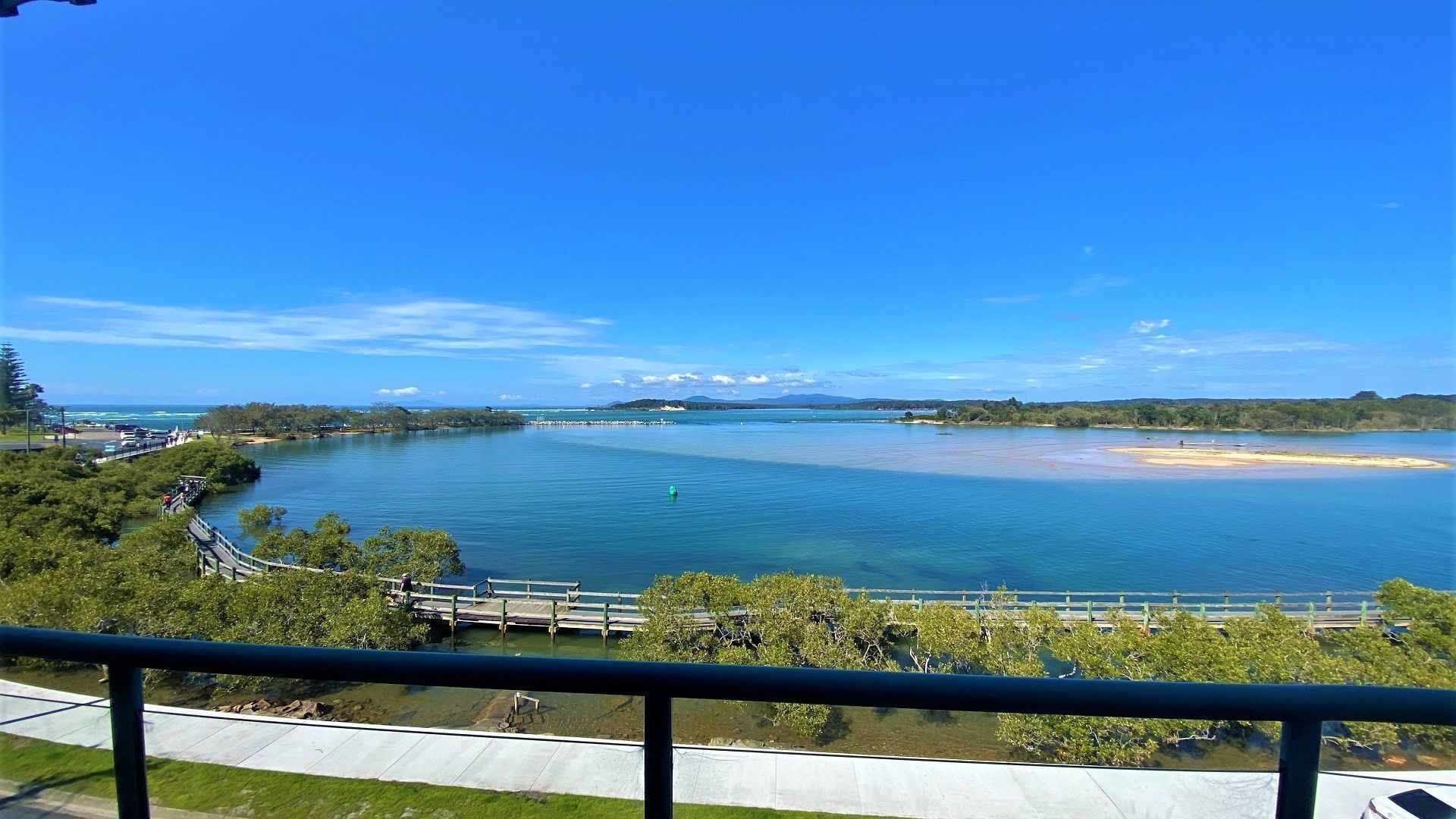 A coastal view with a clear sky, a bridge, and a sandy beach.
