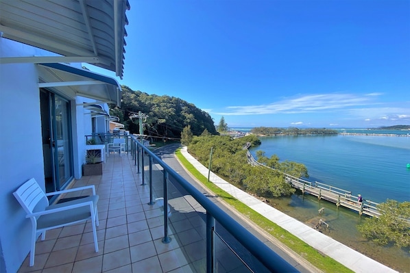 A balcony with a view of a lake, a pathway, and a distant shoreline. - Estuary - Chasing water views? TOP floor unit certainly delivers this & more! (Nambucca Heads)
