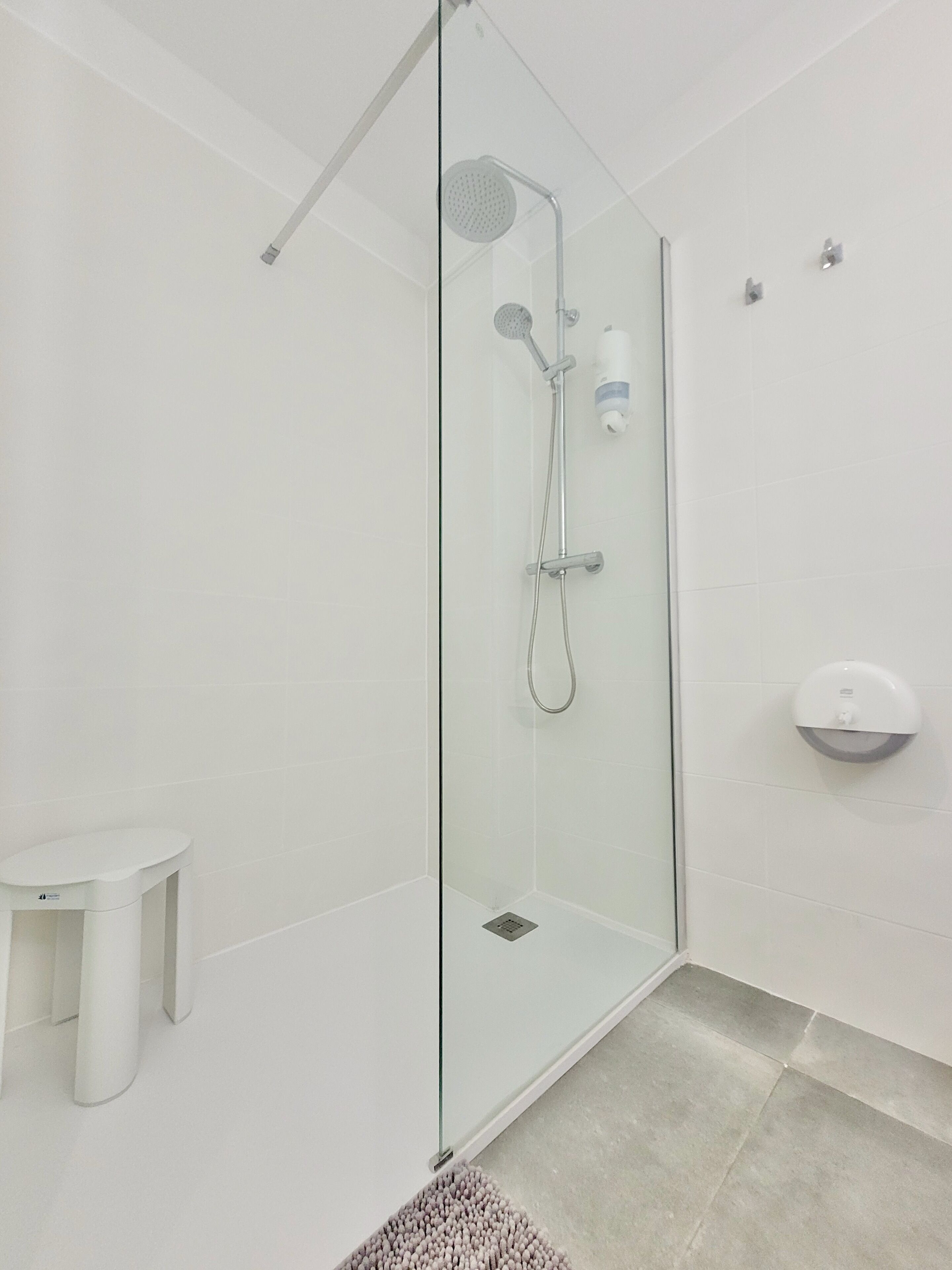 A modern bathroom with a glass-enclosed shower, a white sink, and a small white stool.