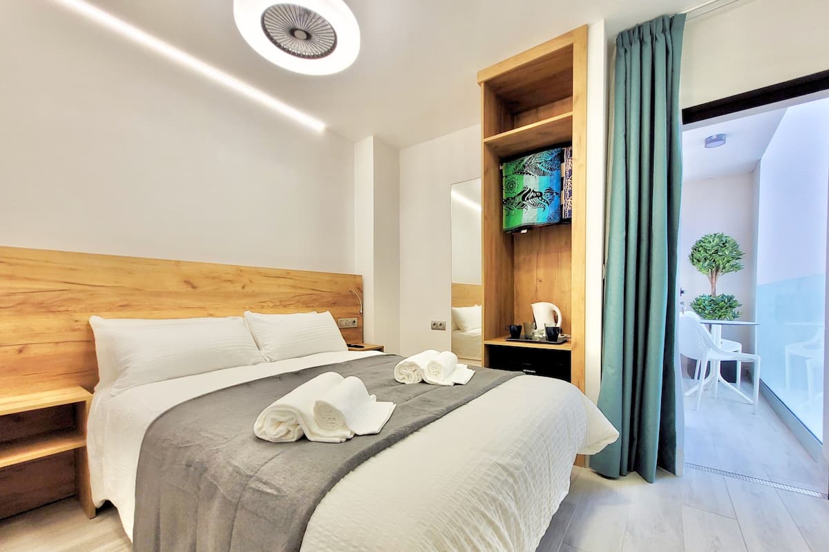 Une chambre d’hôtel moderne avec une tête de lit en bois, un grand lit avec du linge de lit blanc, une table de chevet avec une machine à café et une vue sur le balcon.