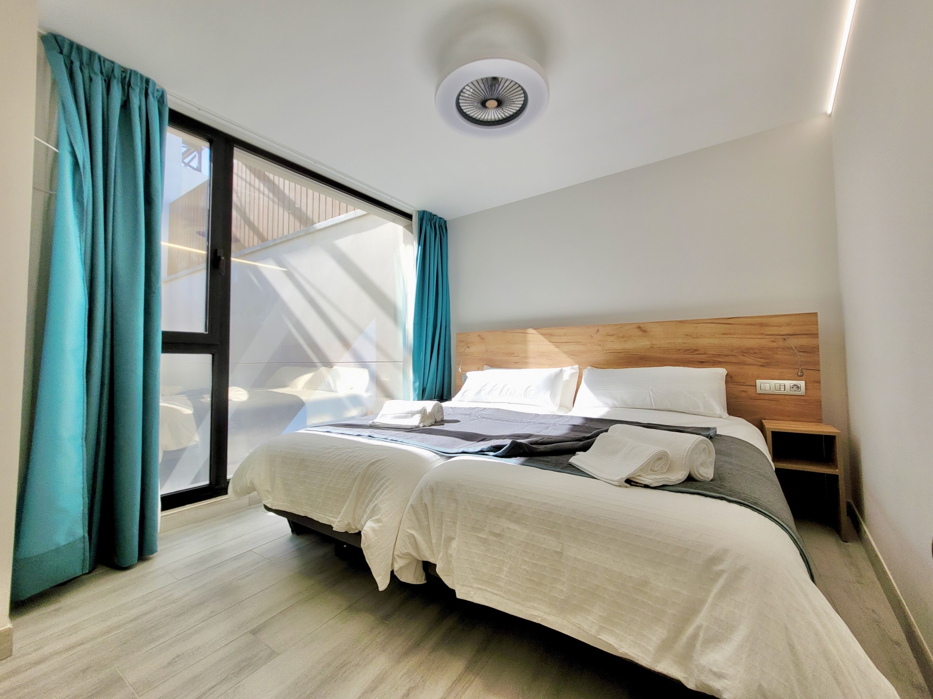 A modern hotel room with a large bed, teal curtains, and a ceiling fan.
