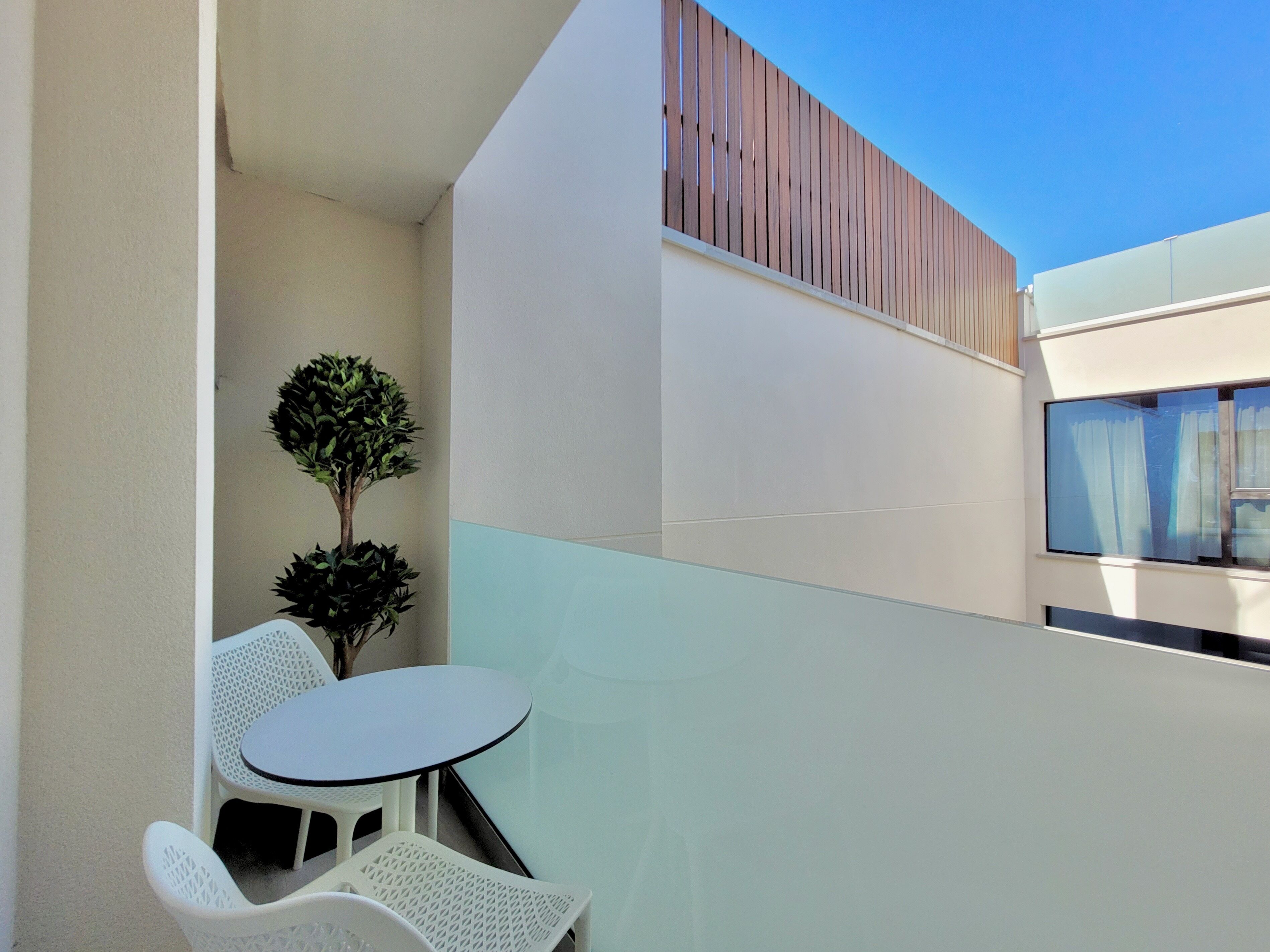 Een balkon met een ronde tafel en twee witte stoelen, een kleine potplant en een houten lambrisering.