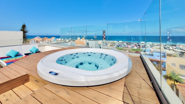 Een hottub op een houten terras met uitzicht op zee en gebouwen.
