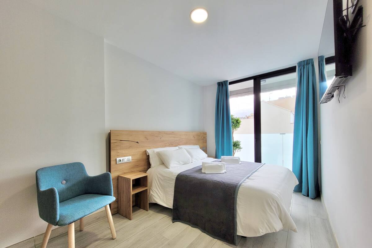 Une chambre d’hôtel avec un lit, une chaise, une table de chevet et une fenêtre avec des rideaux.
